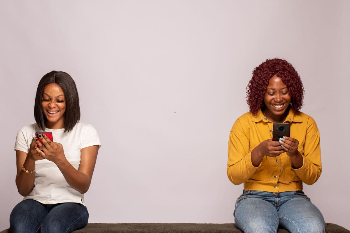Two women looking at a phone together, scrolling a lash tech's Instagram before-and-after posts