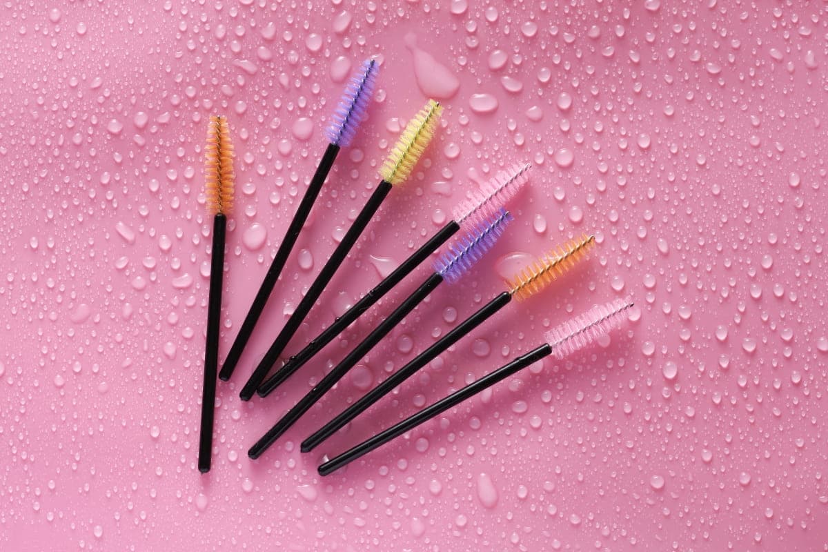 Eyelash extension brushes arranged on a pink background with water drops