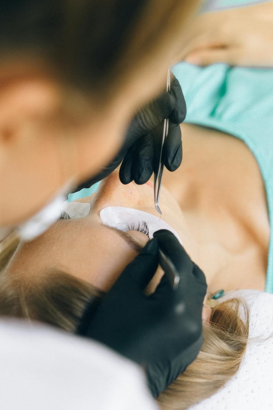 A person wearing black gloves applying lash extensions to a client