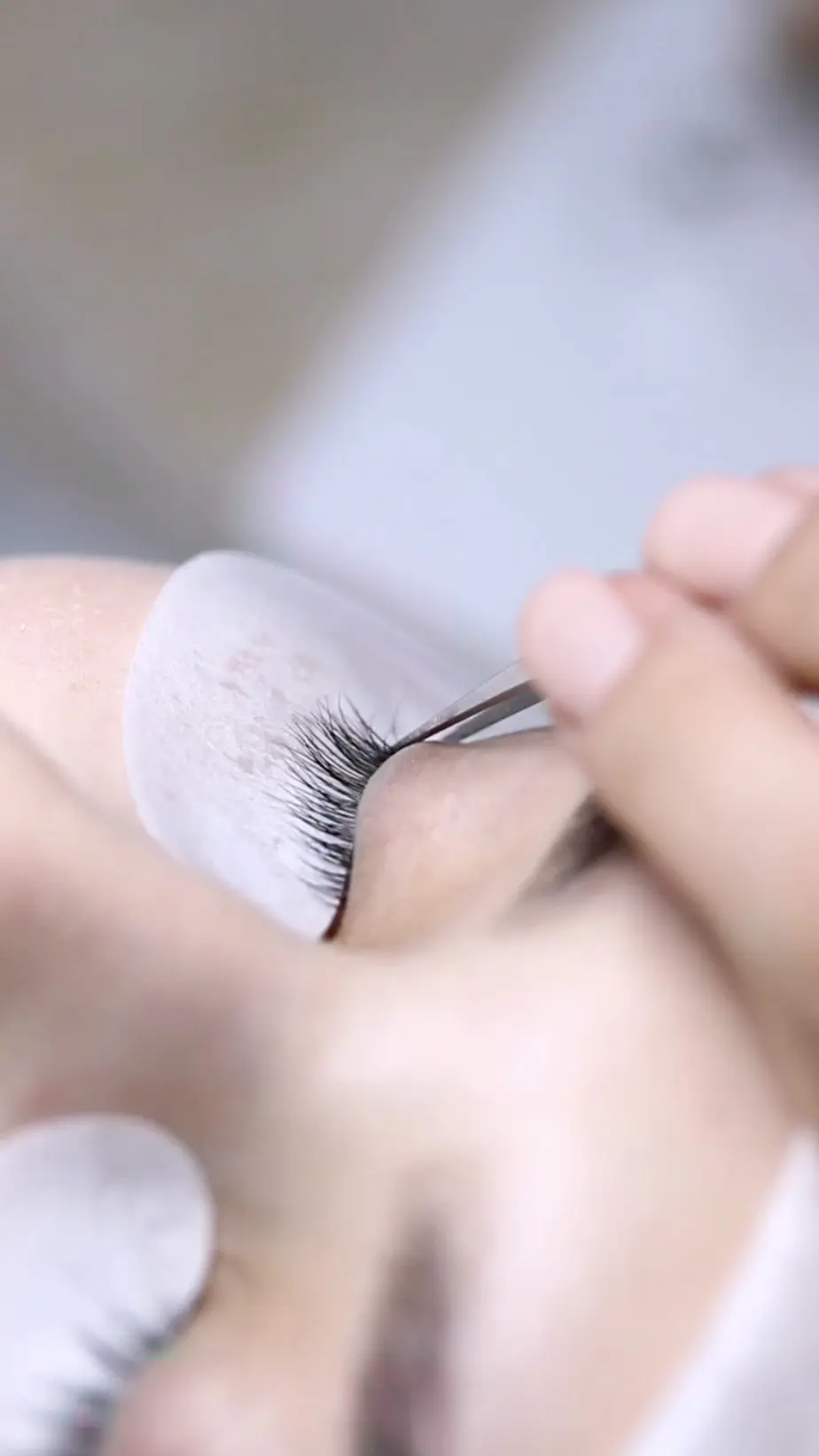 Lash tech working with a client applying eyelash extensions while reviewing the Last Visit Card in SuiteCal